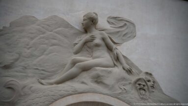 Seated female architectural relief with flowing drapery and theatrical mask detail on the Municipal Theatre façade.