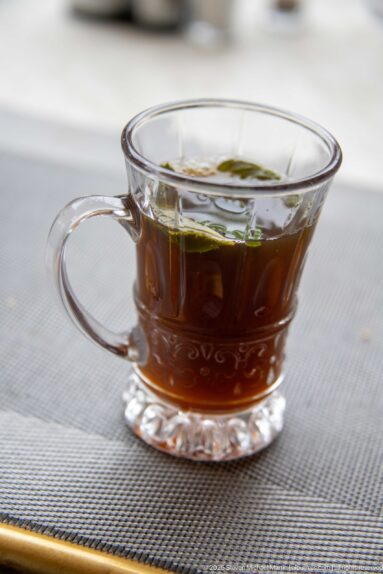Clear handled glass cup filled with amber tea and a small green garnish on a café table.