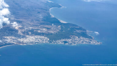 Aerial view of a Tunisian coastal peninsula with dense settlements, pale beaches, inland fields, and blue Mediterranean water.