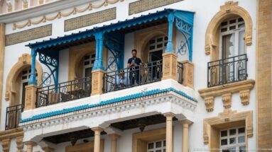 Close view of a blue-painted Hotel Royal Victoria balcony with iron railing, carved stonework, and arched windows.