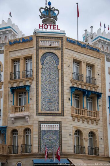 Large blue and ochre ceramic tile panel centered on the Hotel Royal Victoria façade beneath rooftop signage.