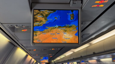 Aircraft cabin display showing Tunis on a western Mediterranean map above rows of passenger seats.