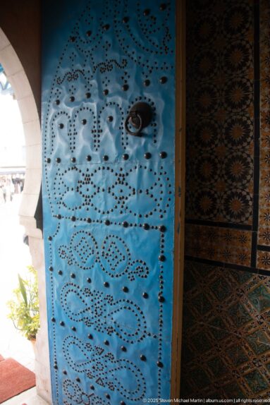 Close view of a bright blue perforated metal door with repeating floral and geometric punched patterns.