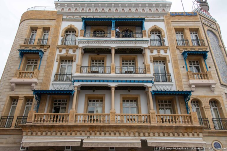 Upward view of the Hotel Royal Victoria façade with stacked balconies, arched openings, and blue-painted awnings.