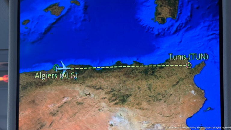 Aircraft map display showing a dotted flight route between Tunis and Algiers along the North African coast.