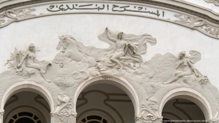 Wide relief on the Municipal Theatre of Tunis with allegorical figures, horses, three arches, and Arabic inscription.