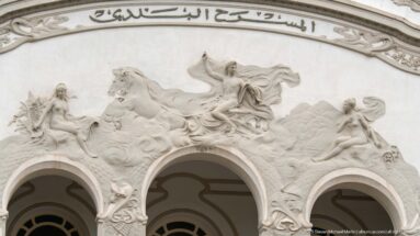 Wide relief on the Municipal Theatre of Tunis with allegorical figures, horses, three arches, and Arabic inscription.