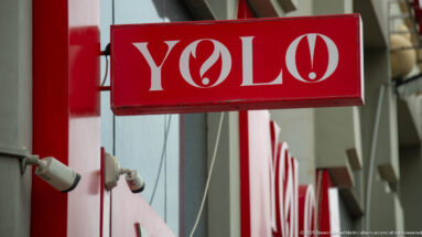 Red projecting storefront sign reading YOLO with white lettering and a flame-like circular symbol.