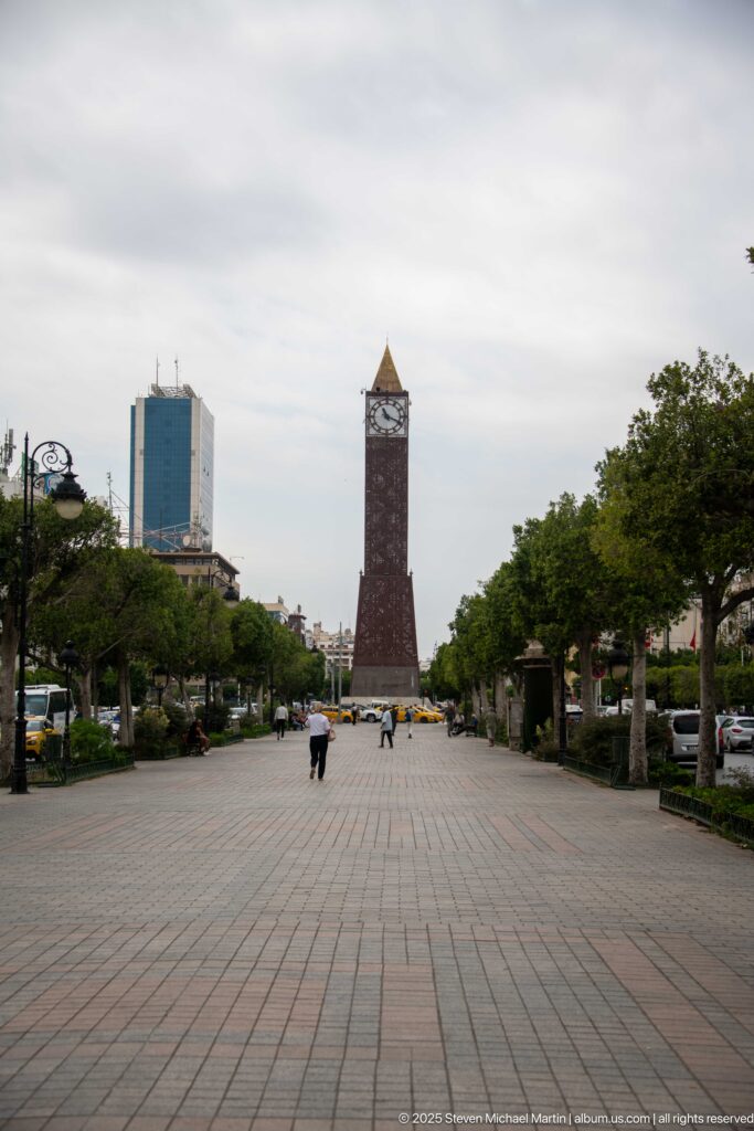 Long paved promenade in Tunis leading between trees and lamps toward the distant Tunis Clock Tower.
