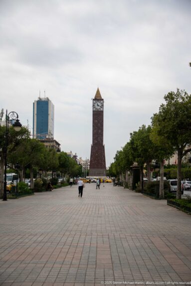Long paved promenade in Tunis leading between trees and lamps toward the distant Tunis Clock Tower.