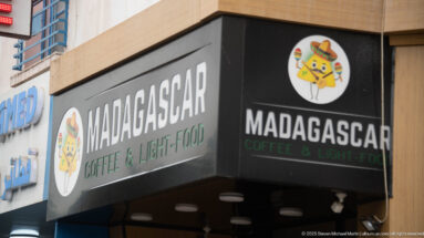 Black storefront sign reading Madagascar Coffee & Light-Food with a colorful circular logo.