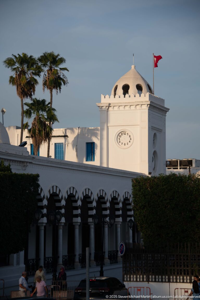 White domed clock pavilion with Tunisian flag above a long arcade of alternating dark and light arches.