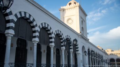 Black-and-white striped arches and columns beneath the white clock tower of Tunisia's Ministry of Finance in Tunis.