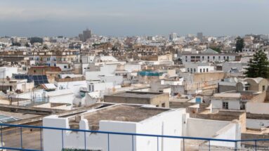 Elevated panorama over dense flat rooftops, satellite dishes, terraces, and pale buildings in central Tunis.