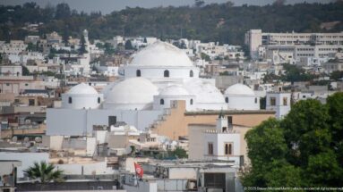 Large white central dome surrounded by smaller domes above dense rooftops in the Medina of Tunis.