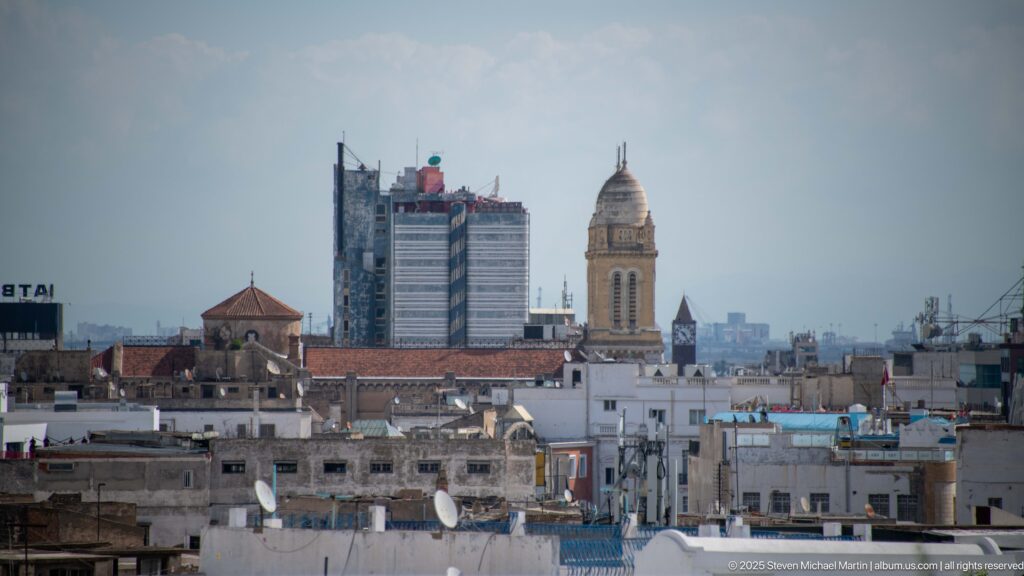Historic Tunis minaret and red-tiled roofs aligned with a modern high-rise under construction in the distance.