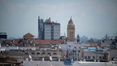 Historic Tunis minaret and red-tiled roofs aligned with a modern high-rise under construction in the distance.