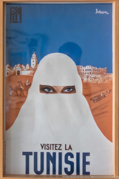 Vintage tourism poster with a white-veiled face, desert settlement, caravan imagery, and text reading Visitez la Tunisie.