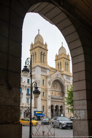 Cathedral of St. Vincent de Paul in Tunis framed by a large stone arch, with twin towers and rose window visible.