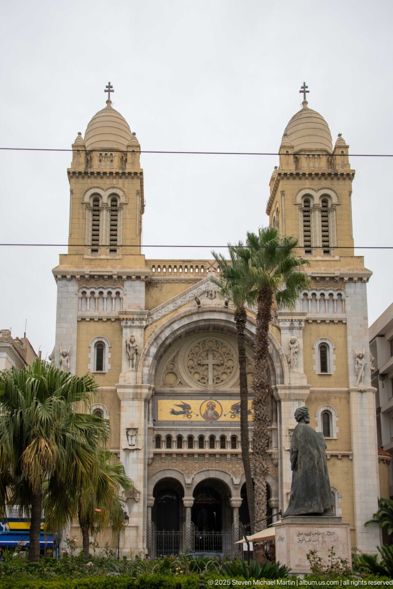 Frontal view of the Cathedral of St. Vincent de Paul with twin towers, rose window, palms, and forecourt monument.