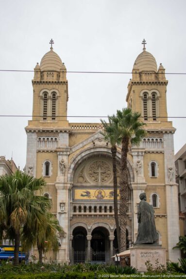 Frontal view of the Cathedral of St. Vincent de Paul with twin towers, rose window, palms, and forecourt monument.