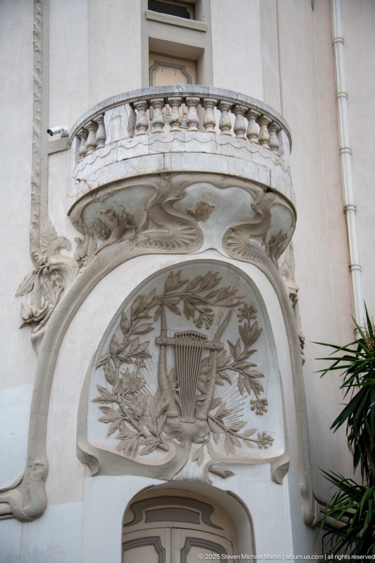 Carved lyre and laurel relief beneath an ornate projecting balcony on a white historic façade in Tunis.