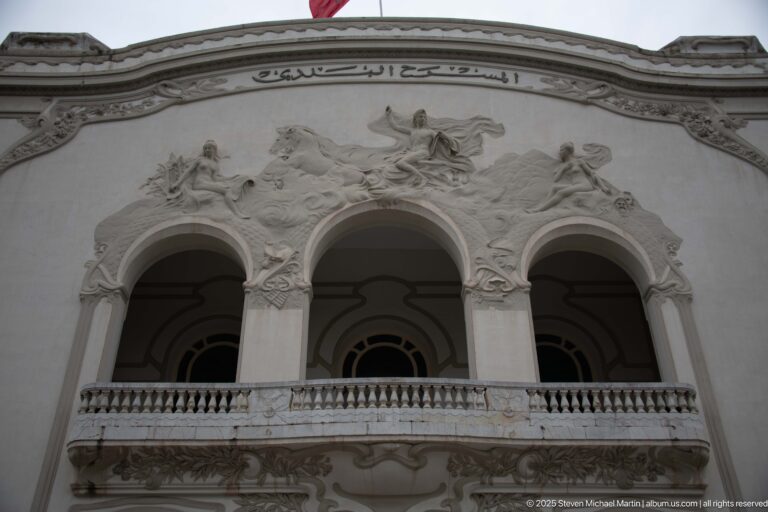 Upper Municipal Theatre of Tunis façade with three arches, balustrade, sculptural reliefs, and Arabic inscription.