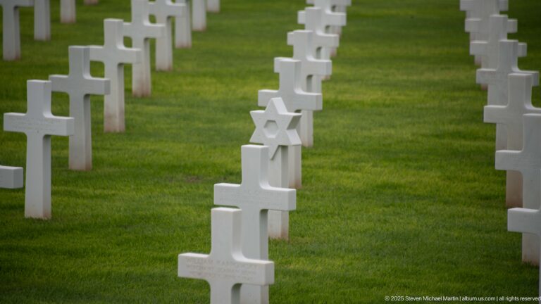 White Star of David grave marker among rows of white Latin-cross headstones on green lawn.