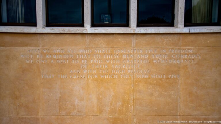 Engraved English dedication inscription cut into pale stone beneath dark window openings.