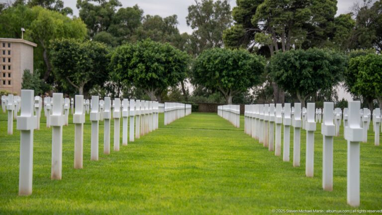Low view along a green aisle between parallel rows of white grave markers.