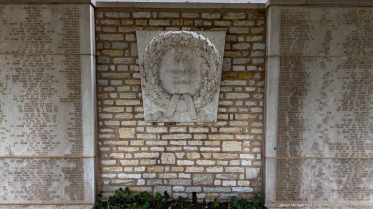 Carved stone wreath with ribbon mounted on a brick wall between tall inscribed name panels.