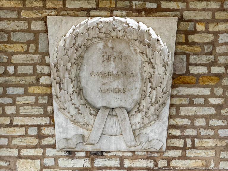 Stone wreath relief inscribed Oran, Casablanca, and Algiers on a masonry wall.