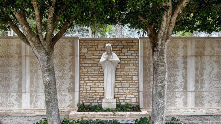 Draped female stone figure centered beneath trees between broad inscribed memorial name panels.