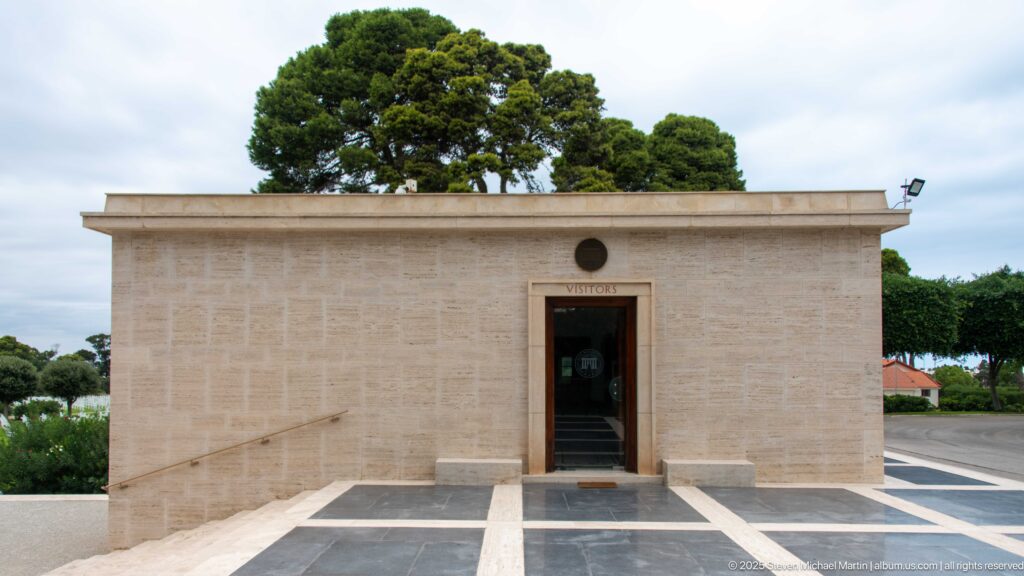 Low pale-stone visitors building with a centered doorway and flat roofline at the cemetery.