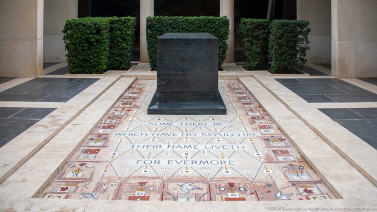 Closer view of a dark pedestal and memorial floor inscription bordered by colored inlaid motifs.