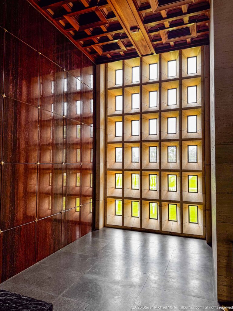 Square-grid translucent window wall with greenish lower panes beside dark wood paneling and a coffered ceiling.