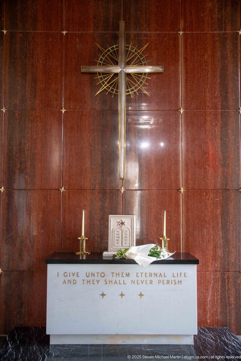 Chapel altar beneath a large cross, with candles and the inscription I give unto them eternal life and they shall never perish.