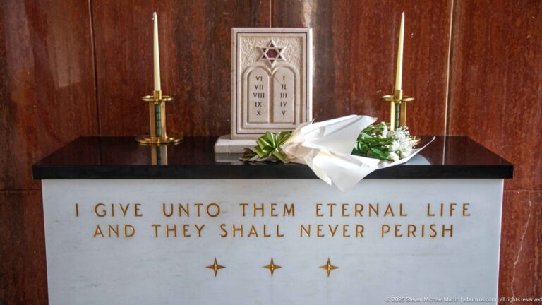 Altar with eternal-life inscription, two candles, white flowers, and a small Star of David tablet with Roman numerals.