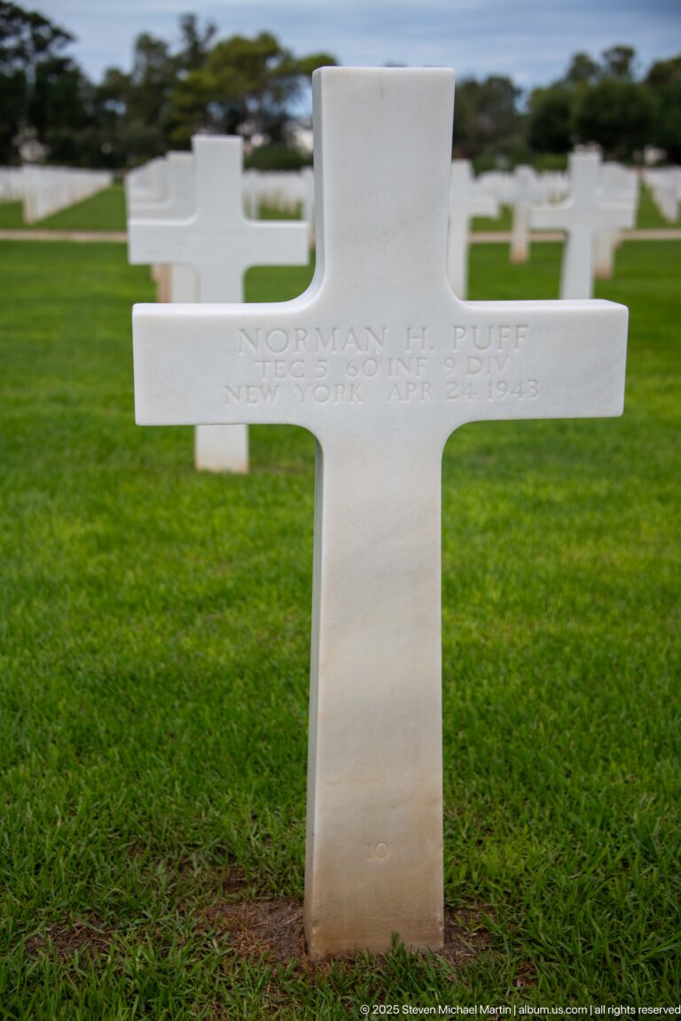 White Latin-cross grave marker for Norman H. Puff of New York on a green cemetery lawn.