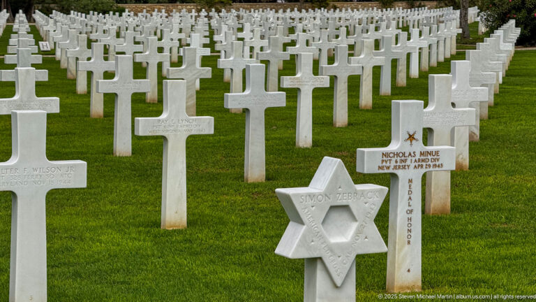 Nicholas Minue Medal of Honor cross beside a Star of David marker among dense rows of white graves.