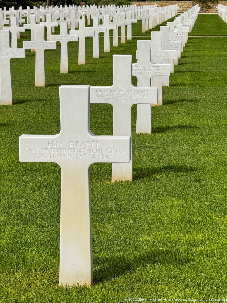 Tom Draper grave marker in front of long aligned rows of white crosses on green lawn.
