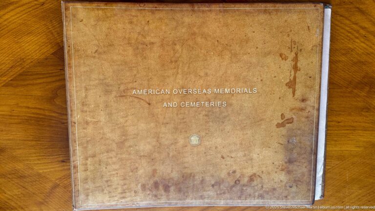 Brown worn book titled American Overseas Memorials and Cemeteries on a wooden tabletop.