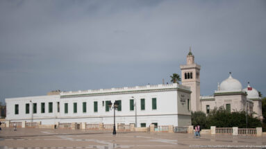 White Bardo Museum palace buildings with green shutters, square tower, domes, and a broad paved forecourt.