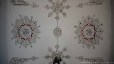 Pale wall with two matching red-and-blue star medallions, fine black geometric drawing, and pendant motifs along the center.