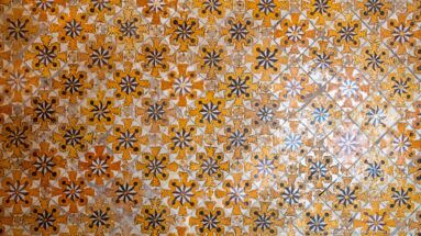 Close view of ceramic tiles forming repeated orange, black, and white floral-star motifs within a diagonal diamond grid.