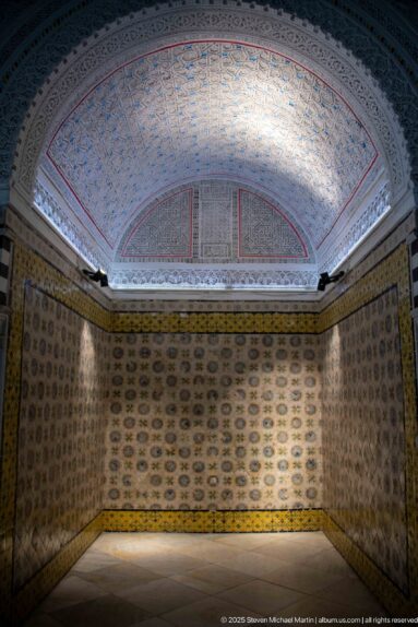 Empty tile-lined room with repeating wall motifs and a shallow painted vault divided into broad red-outlined decorative compartments.