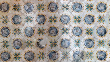 Close view of pale ceramic tiles patterned with large blue radial rosettes and smaller turquoise, yellow, and orange flowers.