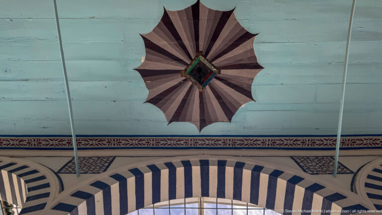 Black-and-white striped arch beneath a dark scalloped radial ceiling rosette on a pale blue ceiling field.