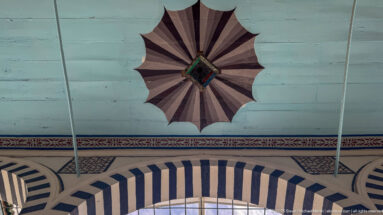 Black-and-white striped arch beneath a dark scalloped radial ceiling rosette on a pale blue ceiling field.