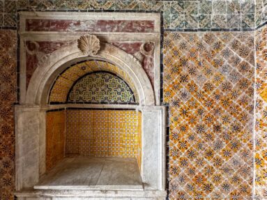 Deep arched marble-framed niche lined with yellow patterned tiles and surrounded by dense multicolored wall tilework.